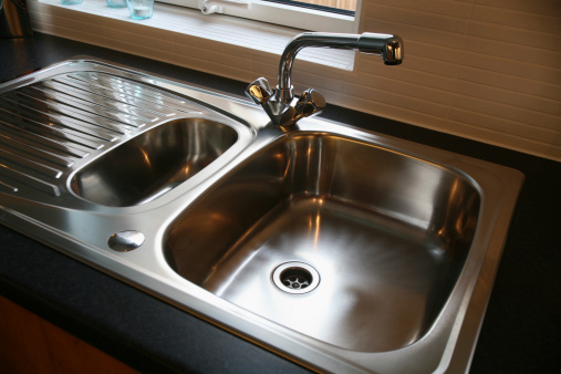 A sink detail shot with an apron sink, green cabinets, black window frame, and a tiled backsplash.