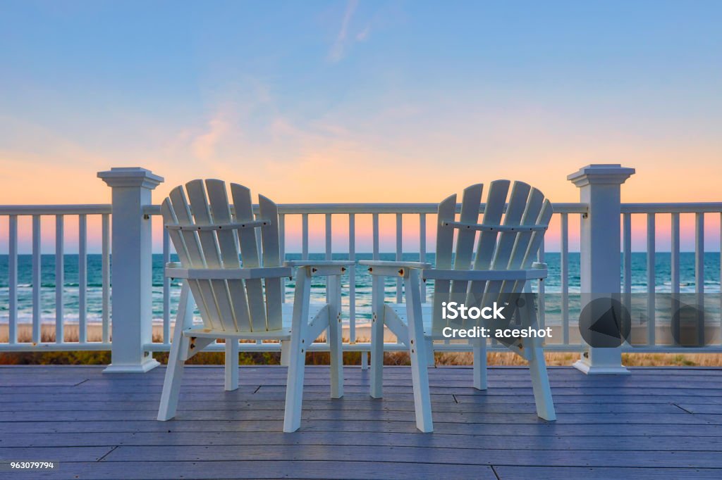 Enjoy the view of the ocean from a chair while on vacation Two empty Adirondack chair on a balcony deck overlooking the beach and the ocean in the Outer Banks of North Carolina Beach Stock Photo
