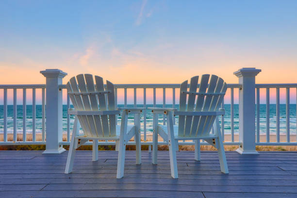 Enjoy the view of the ocean from a chair while on vacation Two empty Adirondack chair on a balcony deck overlooking the beach and the ocean in the Outer Banks of North Carolina promenade stock pictures, royalty-free photos & images