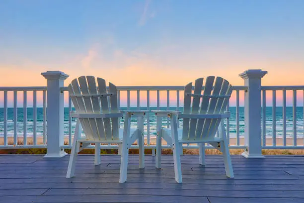 Two empty Adirondack chair on a balcony deck overlooking the beach and the ocean in the Outer Banks of North Carolina