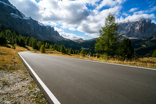 Beautiful mountain road with trees, forest and mountains in the backgrounds. Taken at state highway road in Passo Gardena, Sella mountain group of Dolomites mountain in Italy.