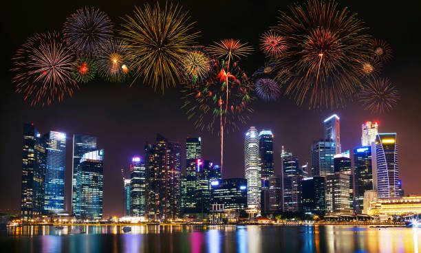 mehreren feuerwerk explodieren hoch in den himmel über moderne gebäude in der stadt. - singapore city stock-fotos und bilder