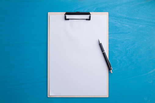 A4 size clipboard with empty copy space paper and pen on blue wood table in workplace. background with blank area for text or message.