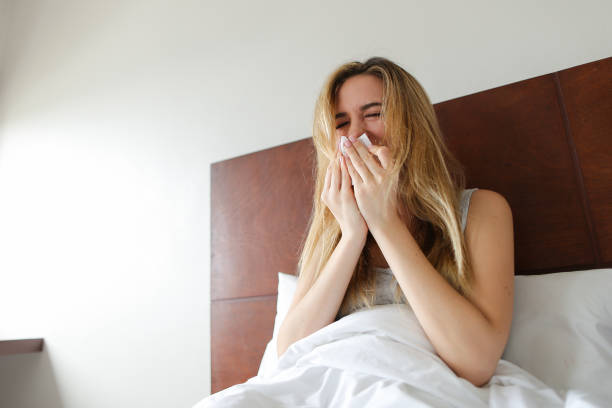 istock Young caucasian woman siitng on bed with running nose and tissues 963102800