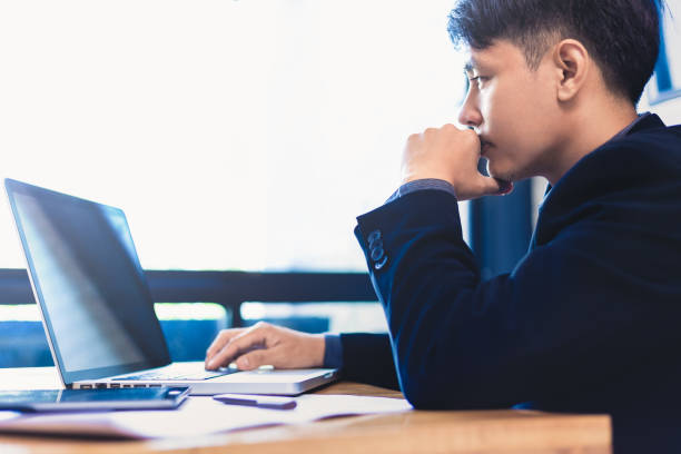 istock Young asian businessman working on his computer in his office near large bright window, selective focus and blur color toning, good for business theme or concept 963108978