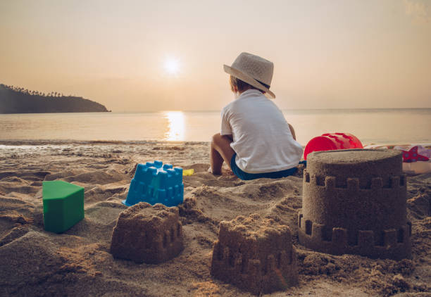 Rear view of a little boy playing with beach toys in sand at sunset.