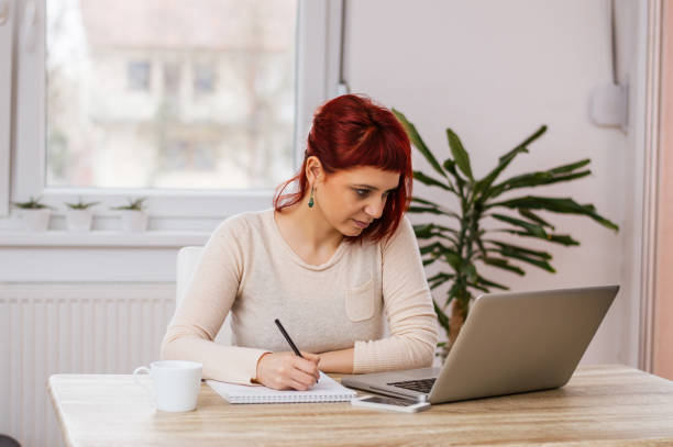 istock Entrepreneur working online with a laptop and taking notes in a notebook in office 963131150