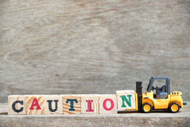 istock Toy forklift hold letter block N to complete word caution on wood background 963140774