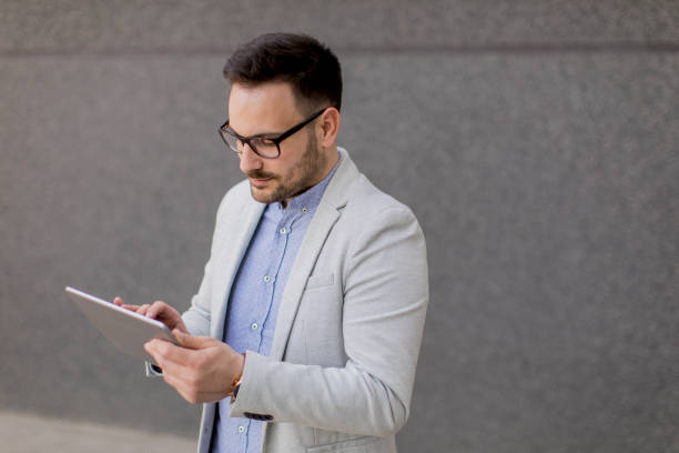 istock Young businessman with digital tablet by the grey wall 963142718