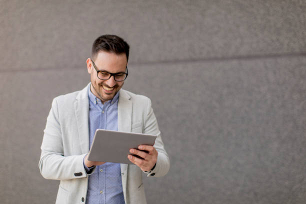 istock Young businessman with digital tablet by the grey wall 963142752