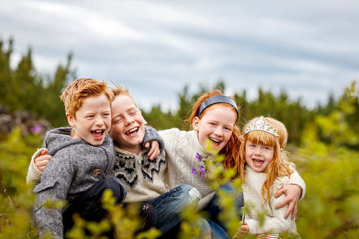 Happy siblings with arms around in forest. Loving brothers and sisters are having fun together. Happy boys and girls are crouching on field.