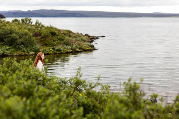 Distant view of girl standing at lakeshore. Little female is enjoying nature's view in forest.