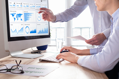 Team of business people discussing digital marketing metrics report and return on investment strategy for advertisement campaign, data analytics dashboard on computer screen in office