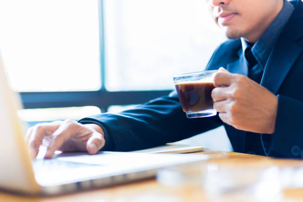 istock Young asian businessman holding a cup of black coffee to drink while working on his computer in his office, selective focus on the coffee cup, good for coffee or business theme 963146618