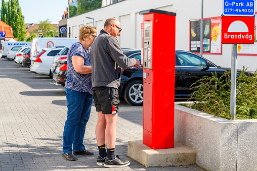 Angelholm, Sweden - May 15, 2018: Travel documentary of everyday life and place. Senior persons standing at a pay station choosing which card to use to pay for their parking space.