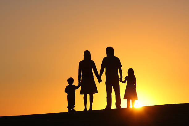 Silhouette of family of four at sunset family silhouetted against setting sun big family sunset stock pictures, royalty-free photos & images