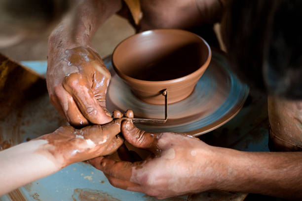 istock Potter's hands guiding child's hands to help him to work with the pottery wheel 963185386