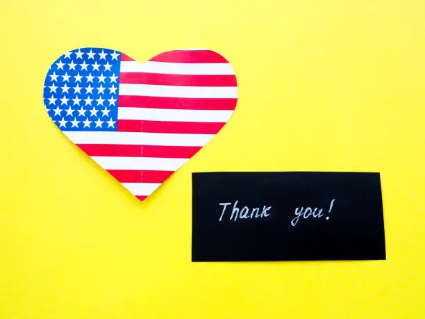 Photo of Thank you sign on a chalkboard with American flag on yellow background, USA