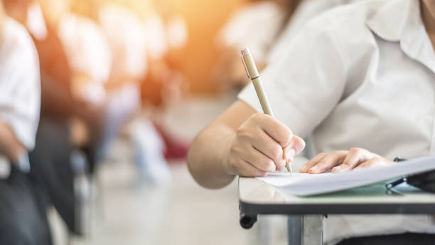 Exam with school student having a educational test, thinking hard, writing answer in classroom for  university education admission and world literacy day concept Exam with school student having a educational test, thinking hard, writing answer in classroom for  university education admission and world literacy day concept exam student university writing stock pictures, royalty-free photos & images