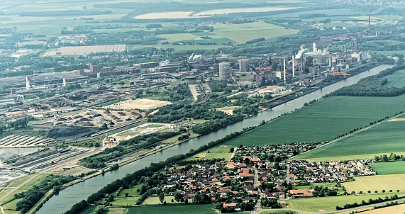 Salzgitter, Lower Saxony, Germany, May 24, 2018: Steelworks on the canal (Salzgitter-Stichkanal) between meadows and fields and a village in the foreground, heavy industry