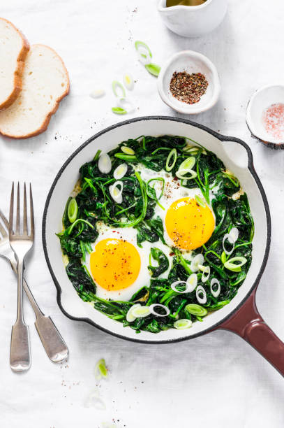 istock Green shakshuka. Fried eggs with fresh spinach, ramson, leek in a cast iron skillet on a white background, top view 963235364