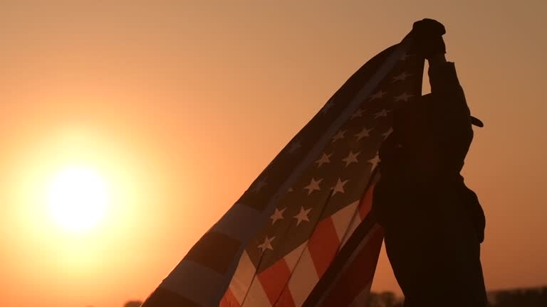 Men Western Wearing Celebrating Independence Day Waving Large American Flag During Scenic Sunset Vista. United States of America Patriot in Cowboy Hat.