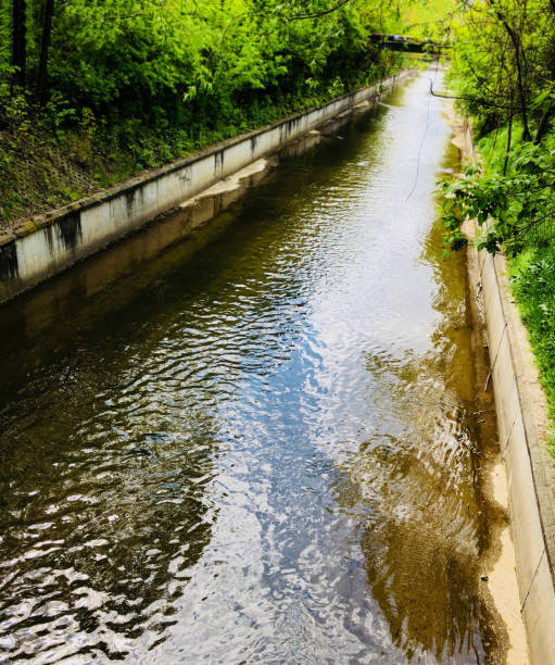 istock calm river in a ditch or gutter under a bridge of pipes in a small town perpective 963294278