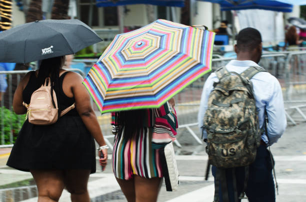Miami - May 25, 2018: Young people gathered for the annual Urban Beach Week celebrations walk down Ocean Drive in South Beach with umbrellas during a rainy Memorial Day Weekend.