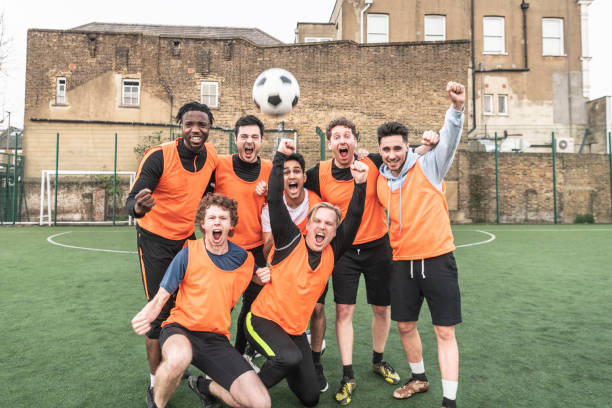 Seven a side football team cheering with ball in the air Candid portrait of young men in football kit with arms in air and shouting as they look towards the camera cheering group of people success looking at camera stock pictures, royalty-free photos & images