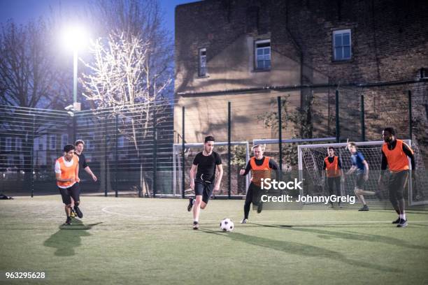 Action Shot Of Footballers On An Urban Pitch At Night With Two Players Running For The Ball Stock Photo - Download Image Now