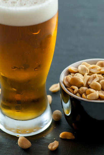 bicchiere di birra e ciotola con arachidi tostate e salate sul concetto di bere sociale ardesia - beer nuts foto e immagini stock