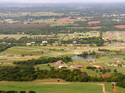 Aerial shot of the outskirts of Oklahoma City with green farmlands and ponds seen from the window of an airplane.