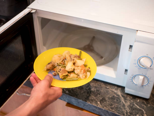 istock close up hand puts plate with fried vegetables in microwave oven 963338514