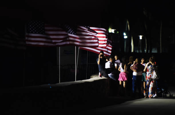 Miami - May 25, 2018: A family gathers for photograph in front of a row of American flags flying along a wall in Lummus Park as part of the Memorial Day weekend celebrations in South Beach.