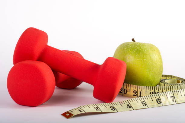 istock Red dumbbell, measuring tape and green apple on white background in studio 963342692