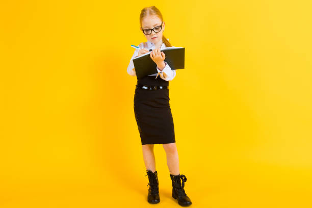 Girl with red hair on a yellow background. A charming girl in transparent glasses writes a pen in her notebook. Portrait of a beautiful girl in a white blouse and black skirt. see through leggings stock pictures, royalty-free photos & images