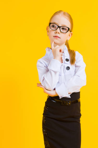 Girl with red hair on a yellow background. A charming girl in transparent glasses put a finger to her chin. Portrait of a beautiful girl in a white blouse and black skirt. see through leggings stock pictures, royalty-free photos & images