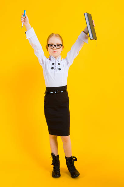 Girl with red hair on a yellow background. A charming girl in transparent glasses holds a pen and a notebook in her hands. Portrait of a beautiful girl in a white blouse and black skirt. see through leggings stock pictures, royalty-free photos & images