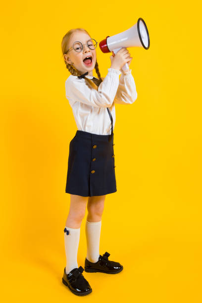 Girl with red pigtails on a yellow background. A charming girl in round transparent glasses screams into the loudspeaker. Portrait of a beautiful girl in a white blouse and black skirt. see through leggings stock pictures, royalty-free photos & images