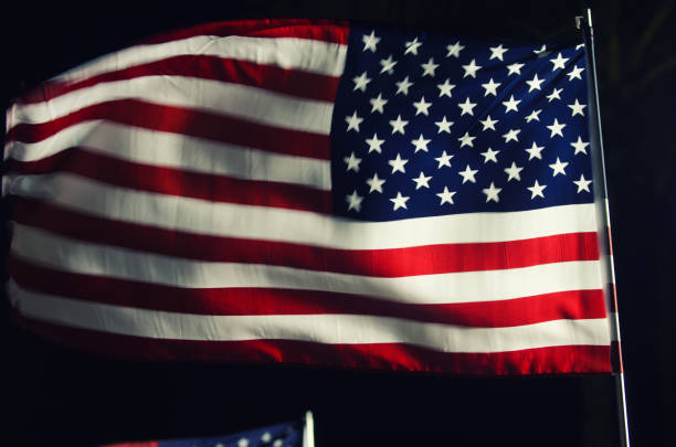 American flag on a flagpole flying in the night wind in motion blur under a dramatic outdoor spotlight