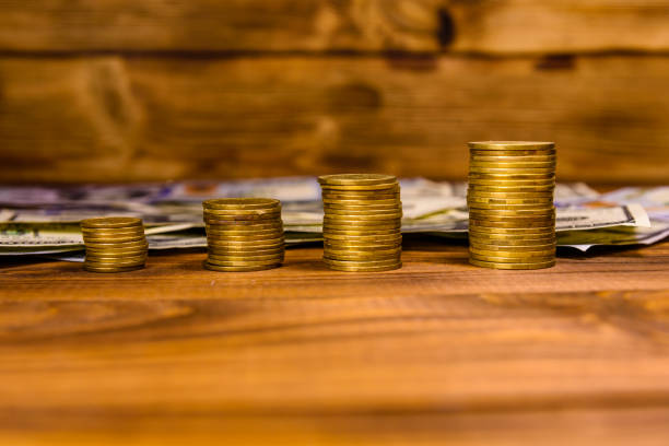 istock Stack of coins and one hundred dollar bills on rustic wooden table 963390962