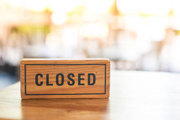 A wooden sign reads closed placed on a table in a coffee shop. The morning light splashes into the back.