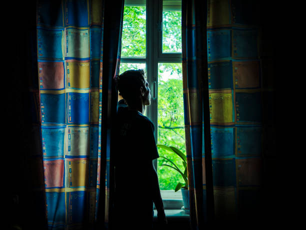 istock alone man silhouette staring at the window closed with curtains in bedroom 963411190
