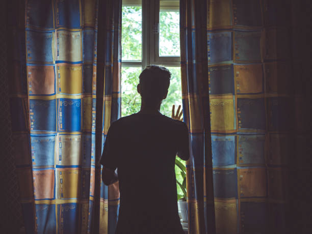 istock alone man silhouette staring at the window closed with curtains in bedroom 963411280