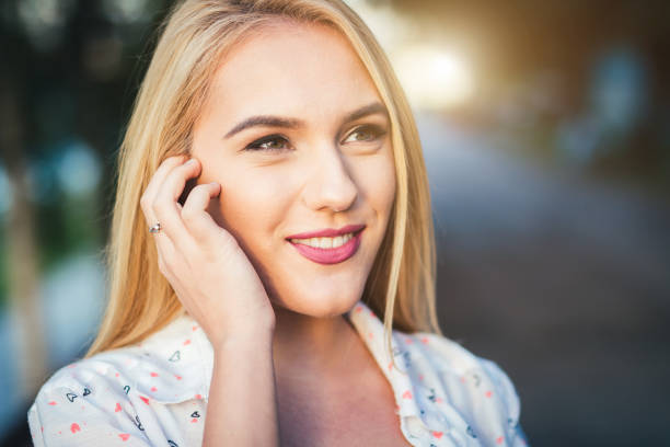 A closeup of a blonde girl outside on a sunny day smiling
