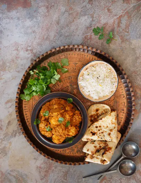 Chicken tikka masala, prepared with tandoori chicken, cooked in a sauce of tomato, yogurt and masala spices. Served with naan bread and pilau rice on vintage copper tray. Top view, blank space