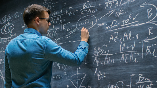 Brillante joven matemático enfoques pizarra grande y acabados escritura matemática sofisticada fórmula / ecuación. photo