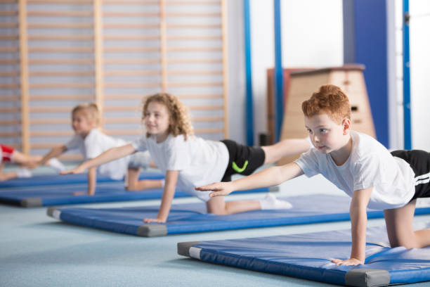 Kids exercising balancing yoga pose Primary school boy and other kids exercising a balancing table yoga pose during extracurricular gym class to help with posture and core body strength physical education stock pictures, royalty-free photos & images