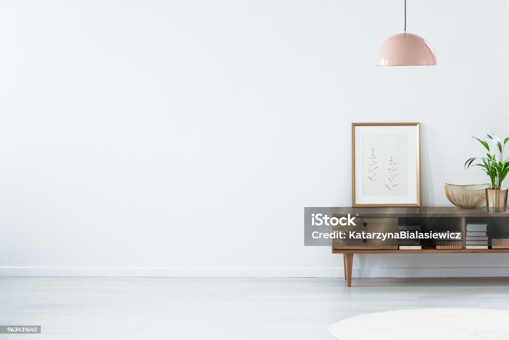 Pink lamp above wooden sideboard Retro pink ceiling lamp above a wooden sideboard in a modern living room interior with an empty white wall and copy space Living Room Stock Photo
