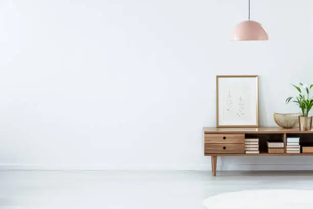 Retro pink ceiling lamp above a wooden sideboard in a modern living room interior with an empty white wall and copy space